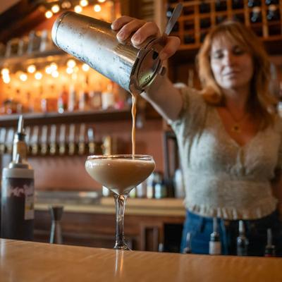 A bartender pouring a creamy cocktail into a coupe glass.