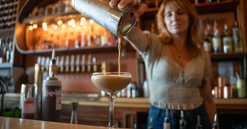 A bartender pouring a creamy cocktail into a coupe glass