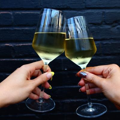 Hands clinking glasses of white wine in a toast.