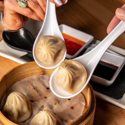 Person holding spoons with soup dumplings above the bamboo steaming basket.