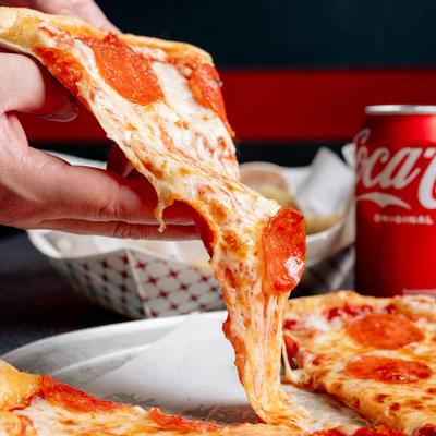 A hand lifting a slice of pepperoni pizza from a metal tray.