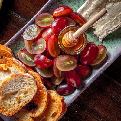 Burgundy board featuring grapes honey and sliced bread.