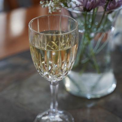 White wine in a crystal wine glass beside a vase of flowers.