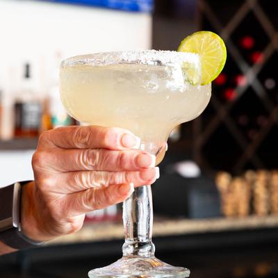 A hand holding a margarita with a salted rim and a lime wedge.