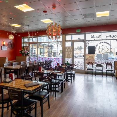 Restaurant dining area with tables, chairs, hanging lights and front windows.