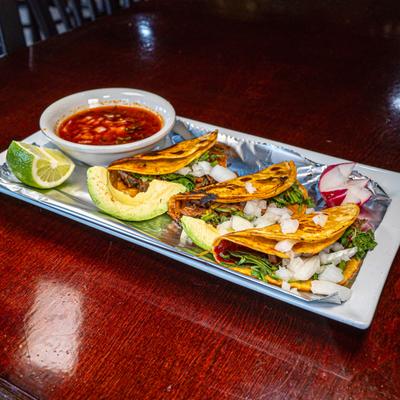 Quesabirria tacos served with a side of consommé, lime, avocado, and radish.
