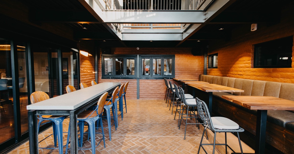 A modern interior with wooden and metal furniture, high ceiling, and brick walls