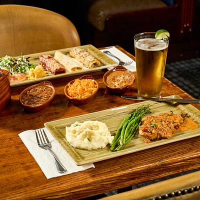 Chorizo Chicken with sides alongside a enchillada, condiments and a glass of beer.