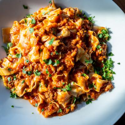 Pappardelle bolognese garnished with fresh herbs.
