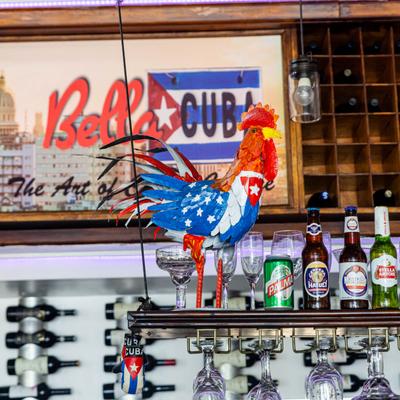 A rooster sculpture painted with American and Cuban flag motifs, beer and wine nearby.