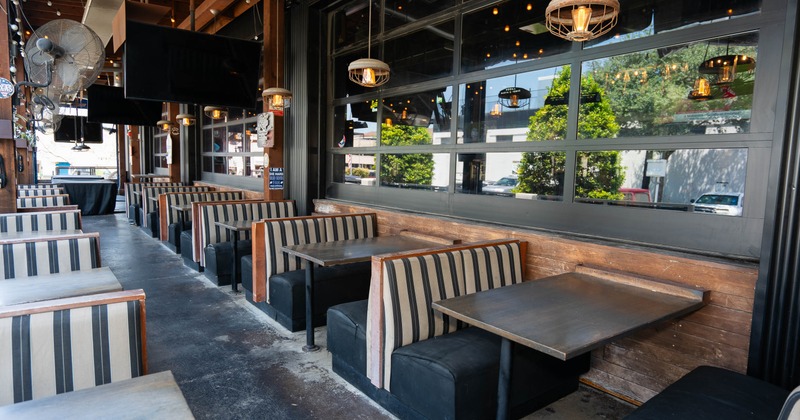 Outdoor patio - striped booth seating, dark wood walls, large glass windows.