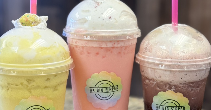 Three different iced drinks in palstic cups, topped with whipped cream