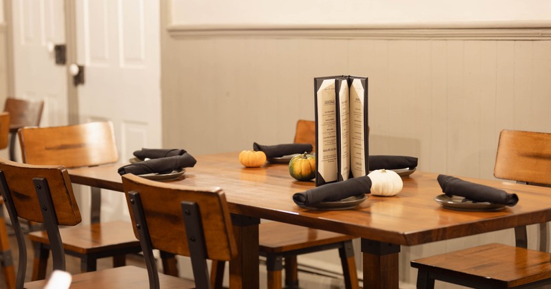 A wooden dining table set with napkins, small pumpkins, and a standing menu