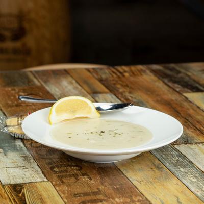 Clam chowder and a lemon slice in a shallow bowl on a rustic wooden table.