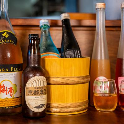 Assorted sake and white yuzu beer bottles with filled glasses on a wooden table.