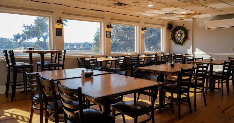 Restaurant interior with wooden tables, black chairs, large windows