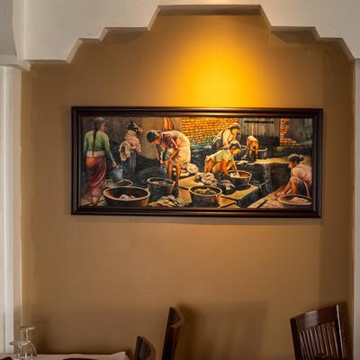 A painting in a dining room, depicts a scene of women washing clothes in a traditional setting.