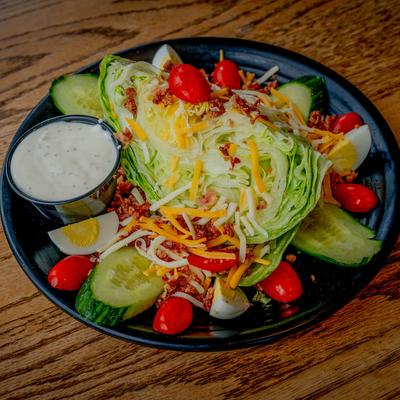 Wedge salad served with ranch dressing on a black plate.
