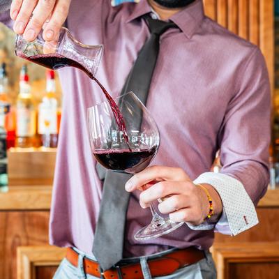 A bartender pouring a glass of red wine.