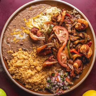 Bacon wrapped shrimp on a bed of onions and bell peppers with cheese, rice, and beans.