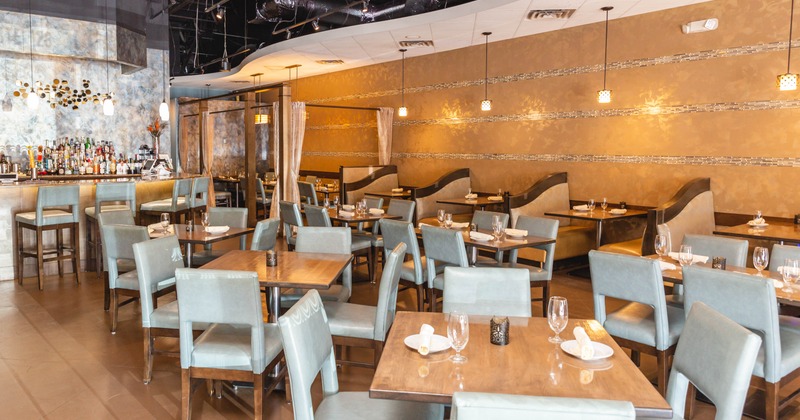 Interior, wooden tables, blue chairs, a bar, and booths along a gold-toned wall