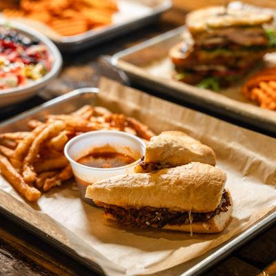 Beef sandwich with served with fries and jus, alongside other dishes on a table.