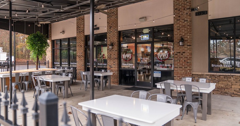 Outdoor seating area of a café with white tables, gray chairs, and a brick facade