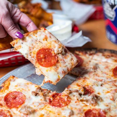A person holding a slice of pepperoni pizza, close up.