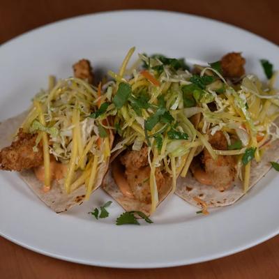 Tacos featuring fried fish, a creamy orange sauce, and a shredded topping.