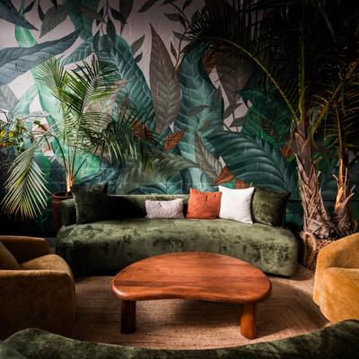 Comfy lounge armchairs and couches with a coffee table in front of a leaf wall mural.