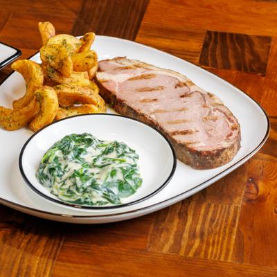 Grilled pork chop accompanied by creamed spinach and seasoned potatoes.