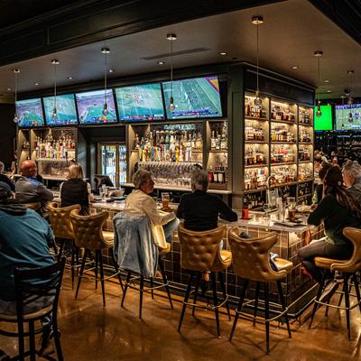 Bar area with guests seated, multiple TVs showing sports, and liquor bottles.