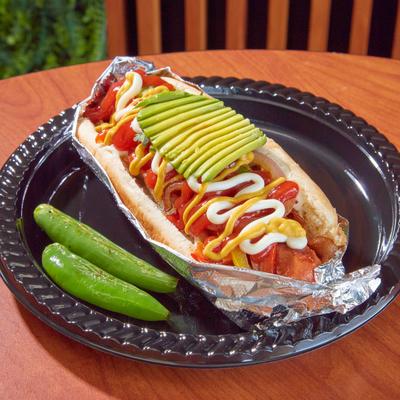 Hot dog topped with avocado, ketchup, mayo, and mustard.