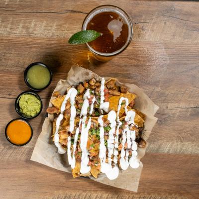 plate of nachos with sour cream drizzled on top with a beer and 2 salsas.