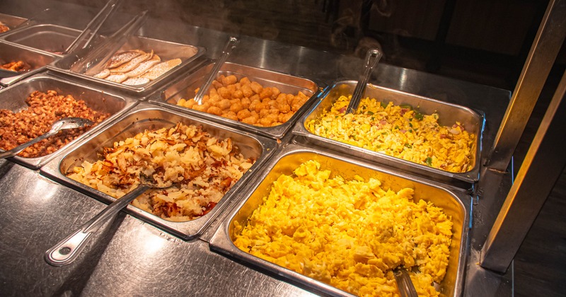 Restaurant buffet setting, featuring hot food pans with steam rising from them