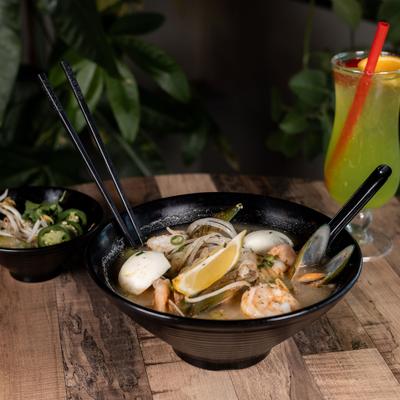 Seafood Ramen served with small bowl of condiments and a cocktail.
