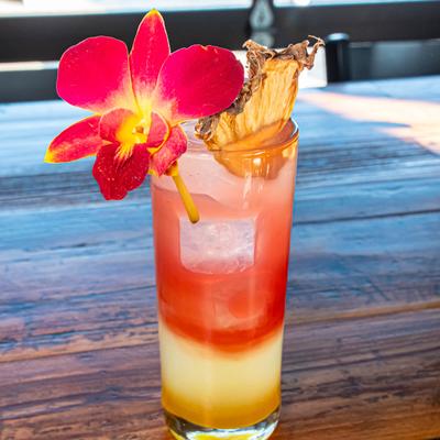 Layered cocktail garnished with a fresh orchid flower and a dried pineapple wedge.