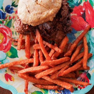 A plated fried chicken sandwich on a cornbread bun and sweet potatoes.