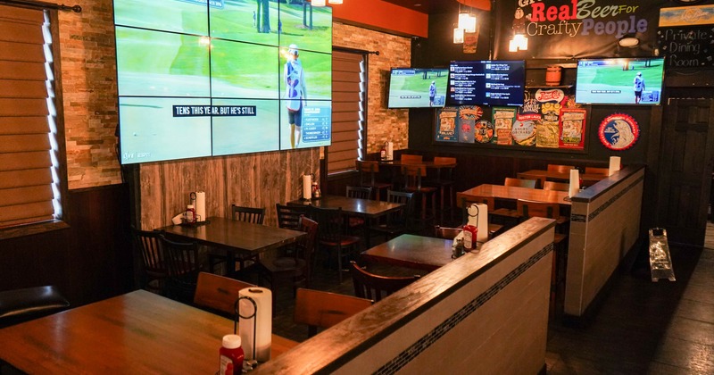 Interior of a sports bar with multiple screens showing a golf game, wooden tables