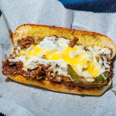 Philly cheesesteak sandwich topped with melted cheese and cheese sauce.