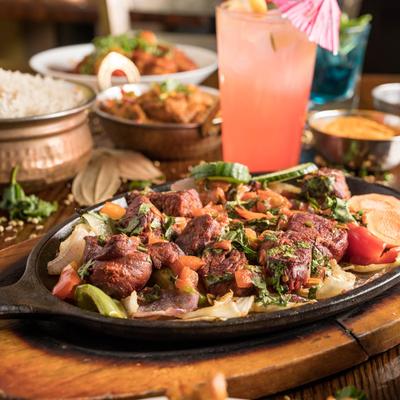 Grilled marinated lamb chunks with veggies, other dishes and drinks in the background.
