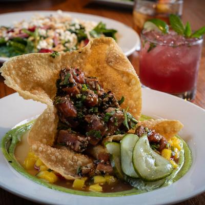Tuna Tartare served in a wonton shell, a salad and a pink cocktail are in the background.