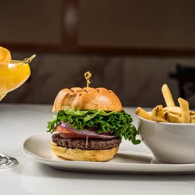 A burger with lettuce, tomato, and onion, served with fries and a mimosa.