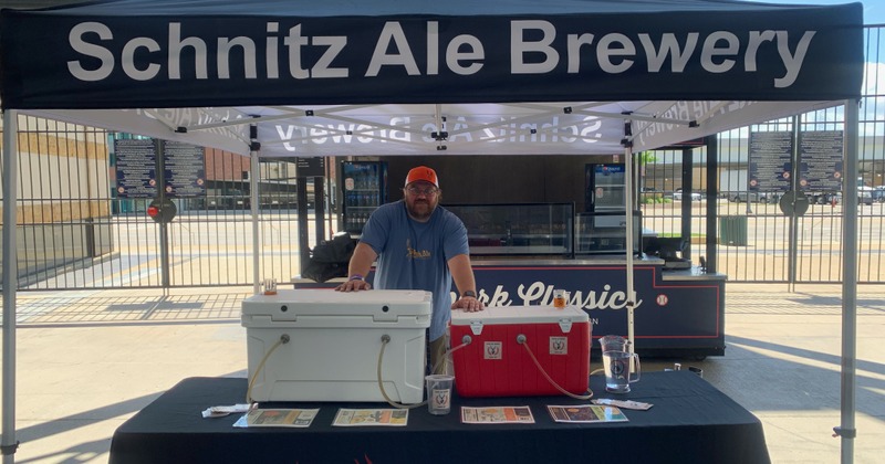 Outside, stand standing under Schnitz Ale Brewery tent by mini fridges