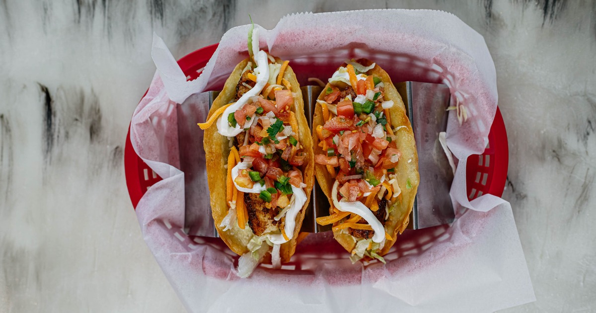 Two hard shell fish tacos in a red basket