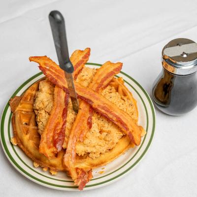 Chicken and waffles with crispy bacon and syrup on the side.