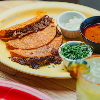 Quesabirria tacos with dipping broth, chopped onions, and cilantro.