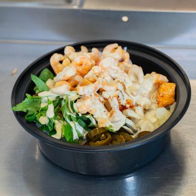 Shrimp bowl with greens, creamy sauce, seasoned chicken pieces, and pickled jalapenos.