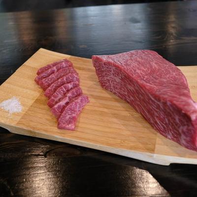 Marbled raw beef arranged neatly on a wooden board on a dark table.
