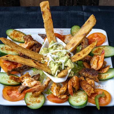 Shrimp and steak platter with guacamole, toasted bread, cucumber, and tomato.